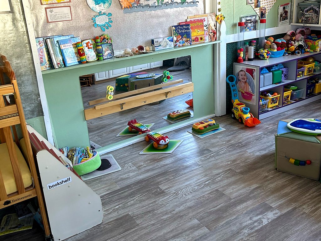 Infant room at a Small Miracles daycare in Tucson with a floor mirror, push toys, books and children's artwork